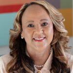 Headshot of Dr. LaTonya Penny. She is wearing a light pink suit with pearls and is in front of a colorful background.
