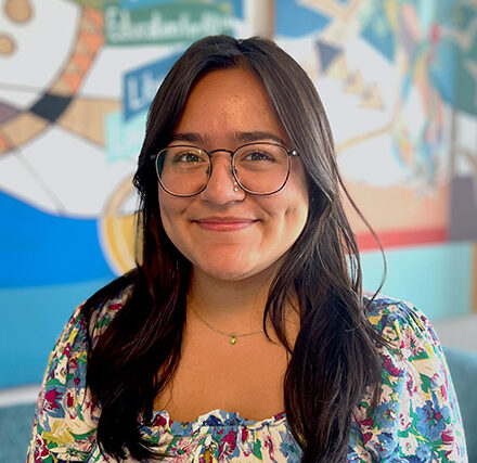 headshot of nayeli gomez. she's wearing glasses and a floral top in front of a colorful mural