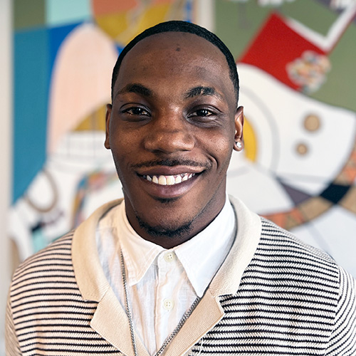 headshot of ryan odom, he's wearing layered collared shirts in front of a colorful mural