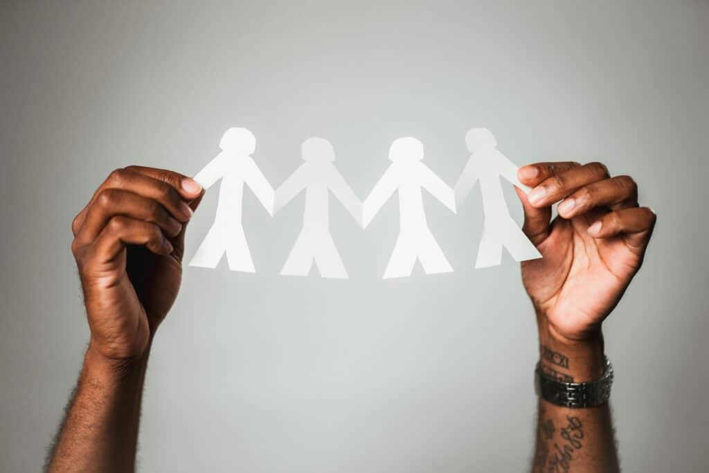 person with brown skin holds a paper chain of 4 human shapes between their hands