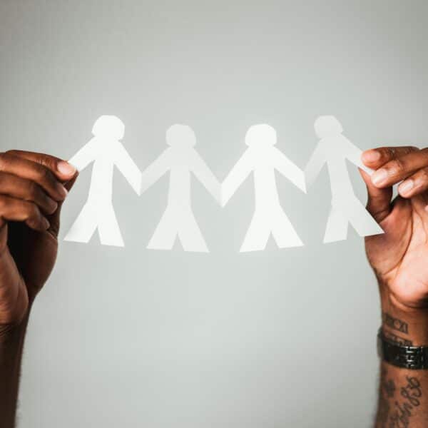 person with brown skin holds a paper chain of 4 human shapes between their hands