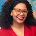 Marion Johnson headshot - She's wearing red glasses and a red shirt against a mural backdrop